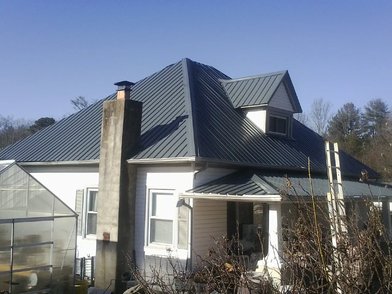 Dark blue standing seam metal roof on a white farmhouse with dormer — Slate & Tile Roof Repair by Roofing Brothers in Beresford