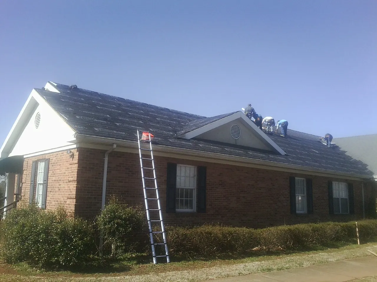 Crew tearing shingles off a brick ranch roof with a ladder set — Metal Roof Repair work by our crew in Beresford