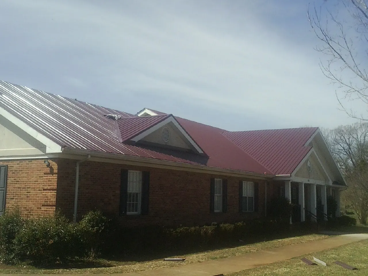Red metal roof with gabled entries on a long brick building, from a Hail Damage Roof Repair job in Beresford