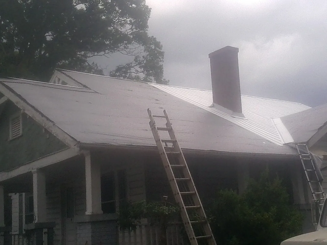 Ladders against a metal roof on an older home with a brick chimney in Beresford