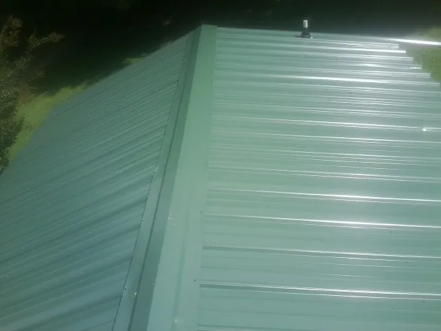 New green metal panels meeting at the ridge of a roof — Flat Roof Repair work by our crew in Beresford