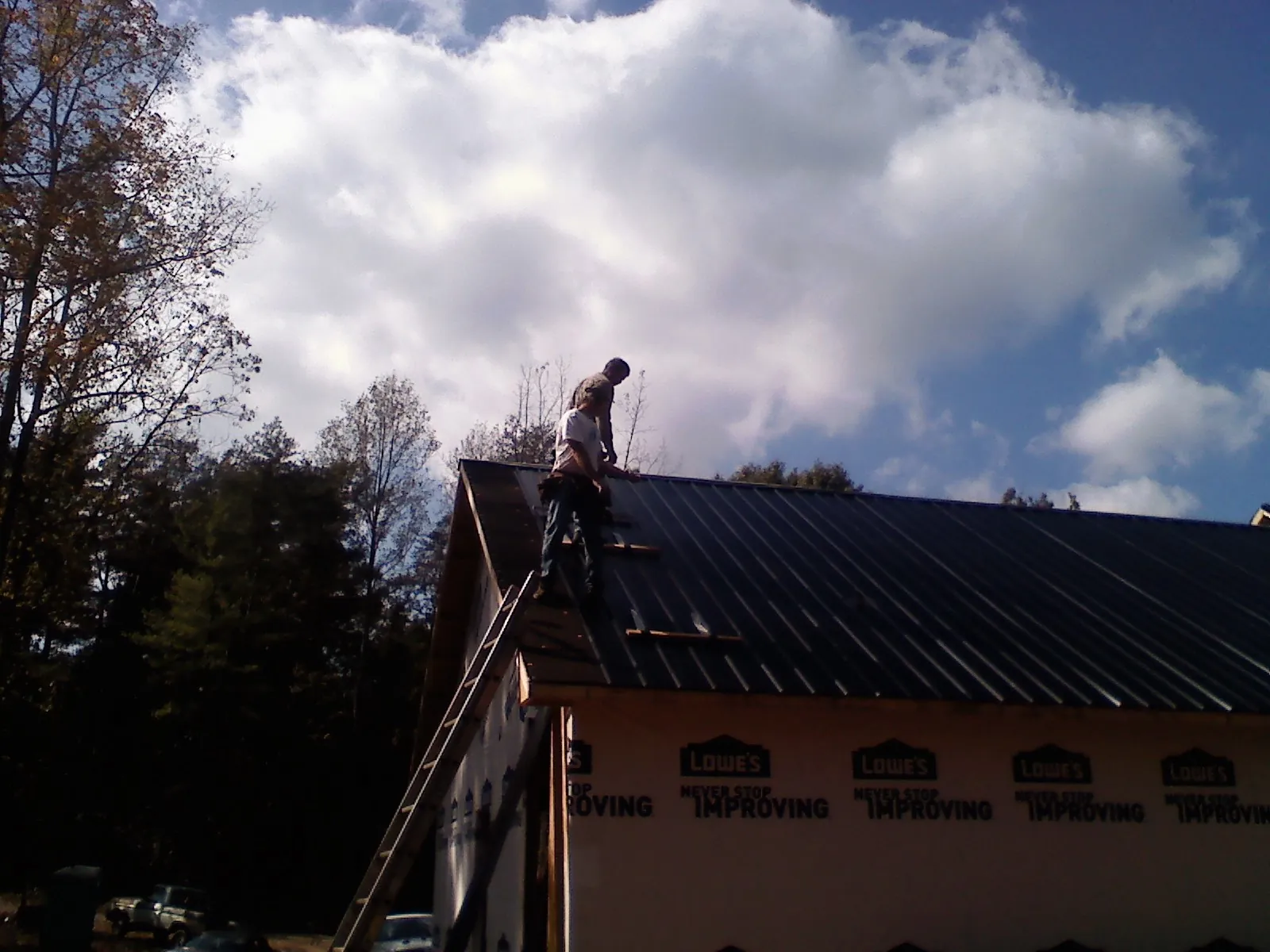 Roofer fastening dark metal panels high against a cloudy sky, from a Roof Inspection job in Beresford