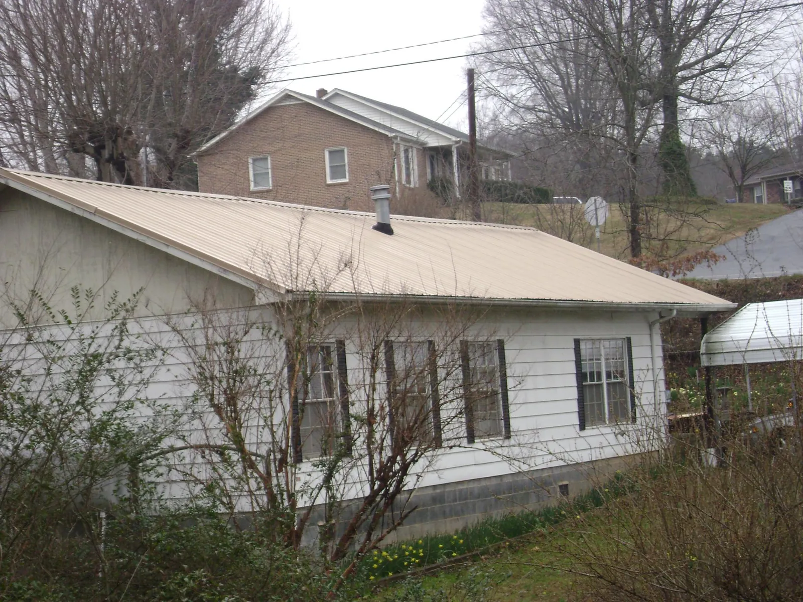 Tan metal roof on a white sided house set into a hillside — Commercial Roofing by Roofing Brothers in Beresford