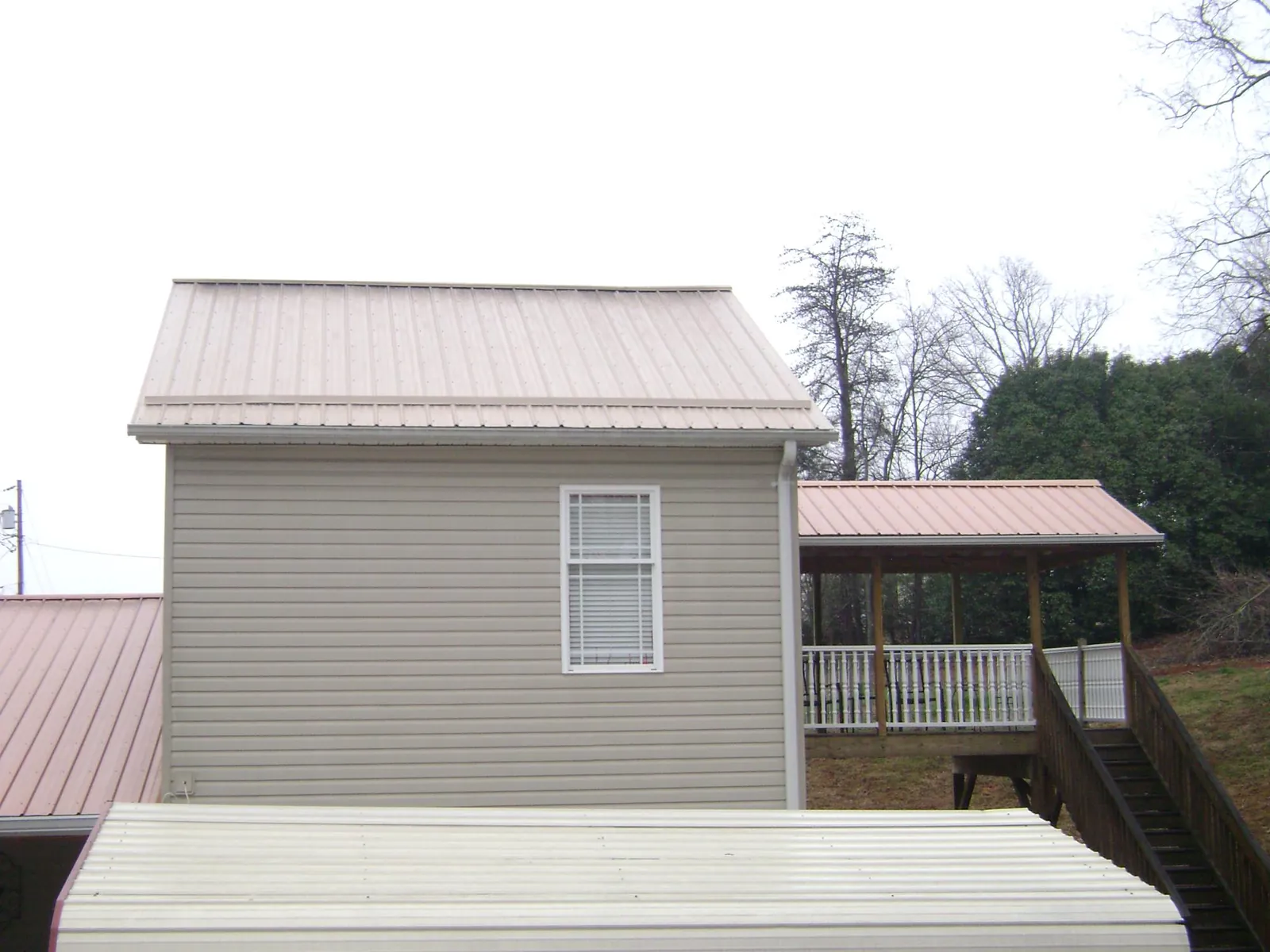 Tan metal roofs on a two story addition and attached porch, from a Roof Replacement job in Beresford